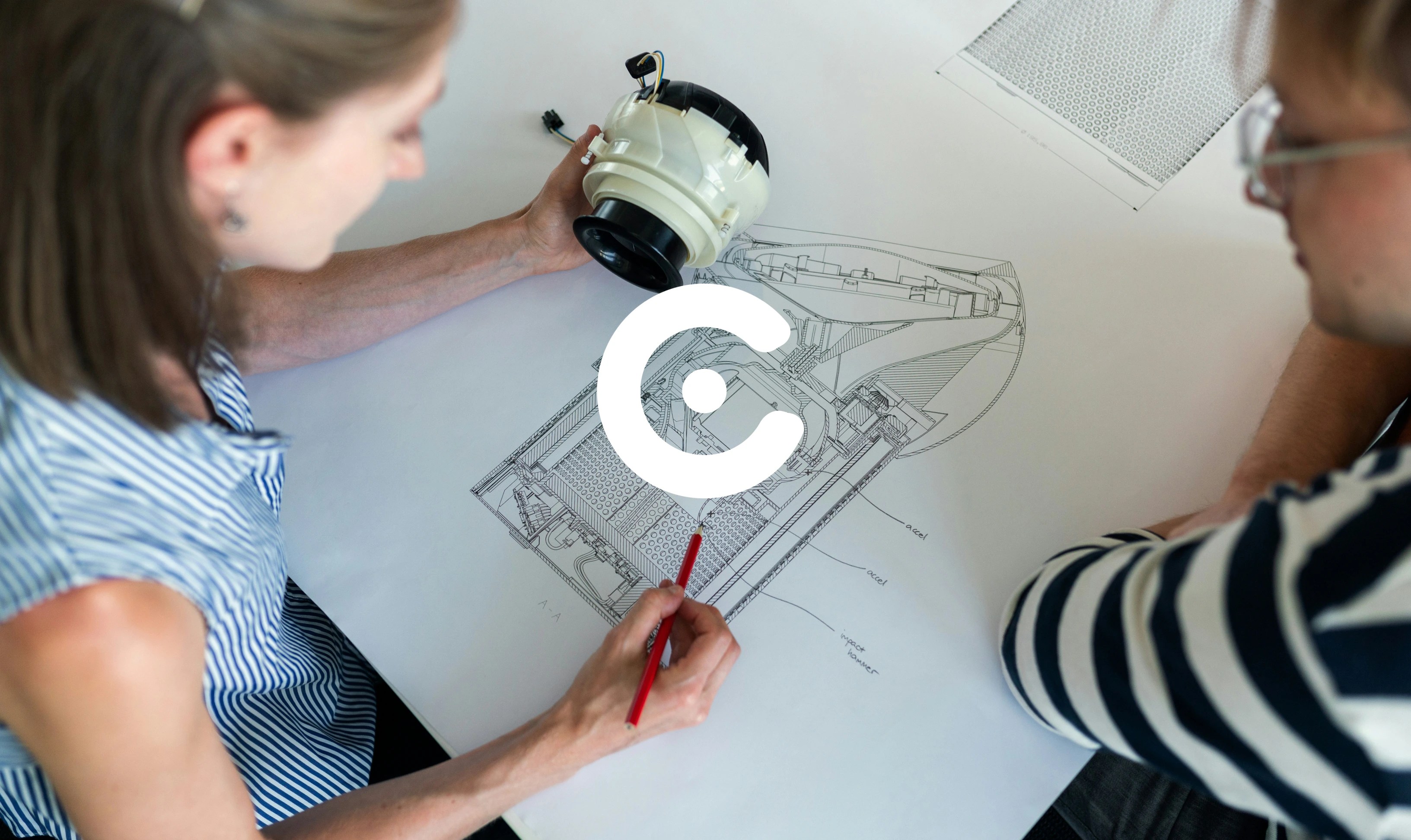 Two engineers review a technical cross-section drawing while holding a mechanical component on a desk.