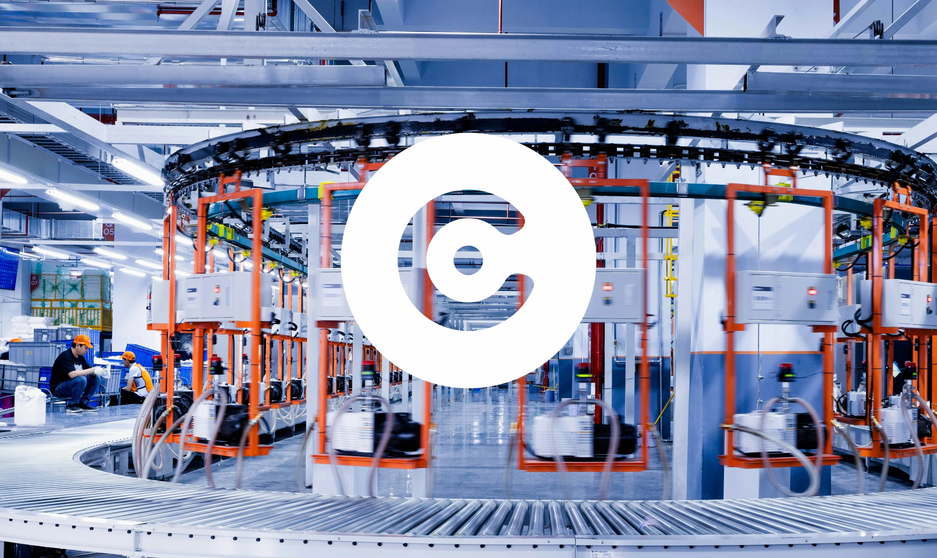 Automated factory interior with a circular overhead conveyor system carrying equipment in orange frames, workers visible in the background, and a large white circular logo overlaid at the center.