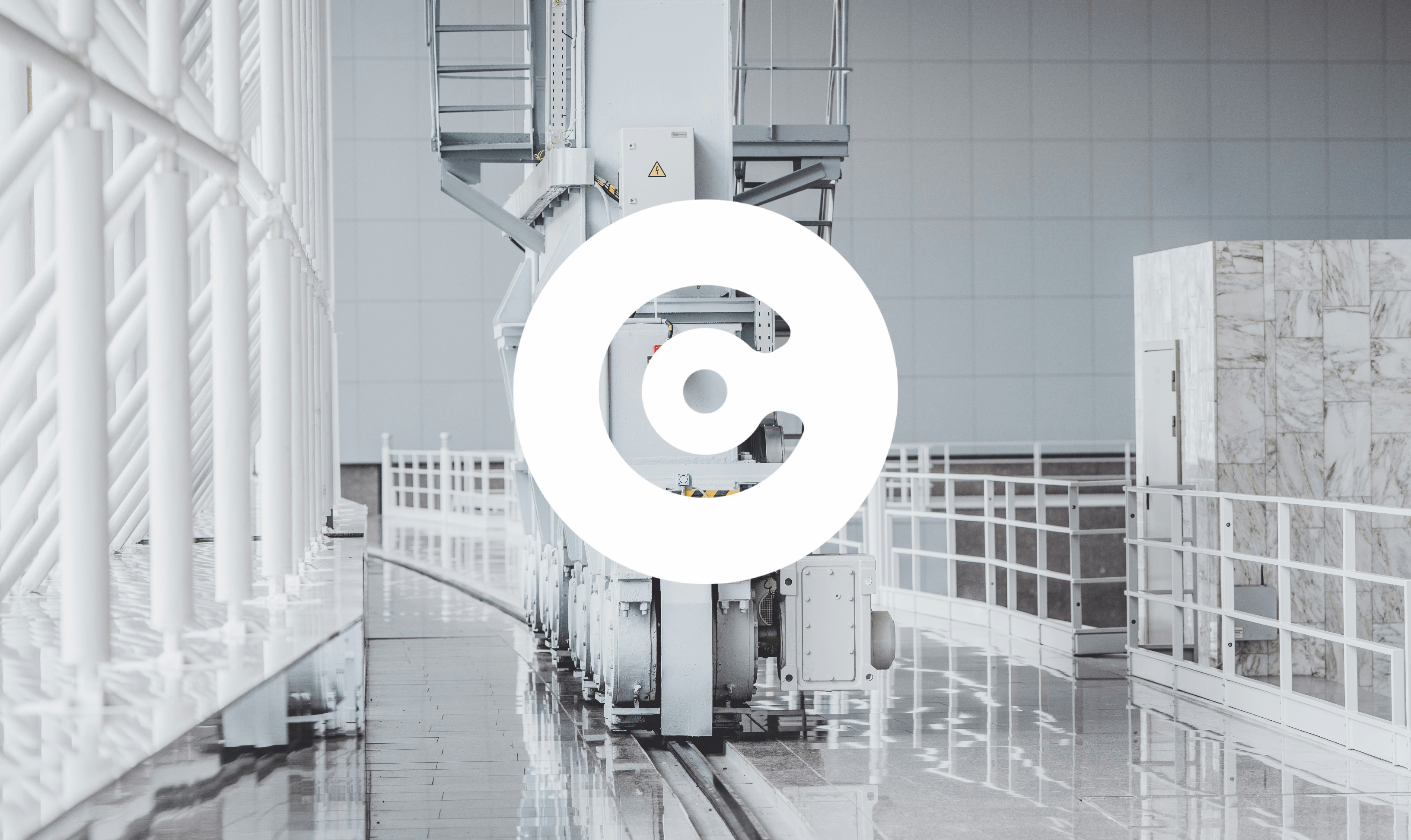 Industrial interior with a rail-mounted machine centered on a glossy floor, surrounded by white railings and tiled walls in a clean, modern facility.