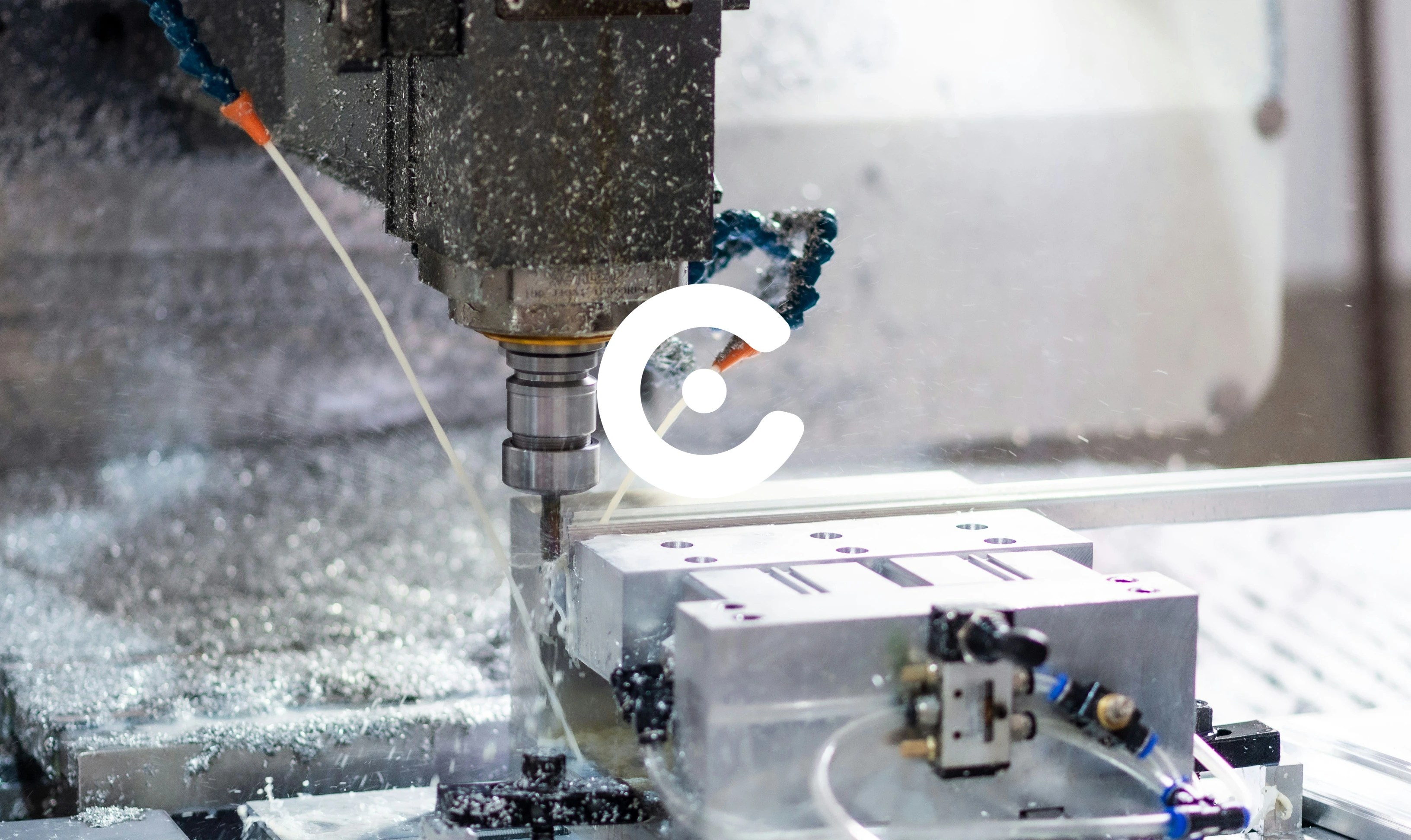 Close-up of a CNC milling machine cutting a metal block, with coolant spraying and metal shavings visible during the machining process.