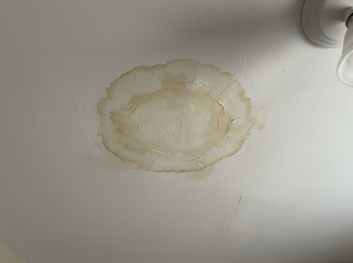 Circular water stain and cracks on white ceiling next to a light