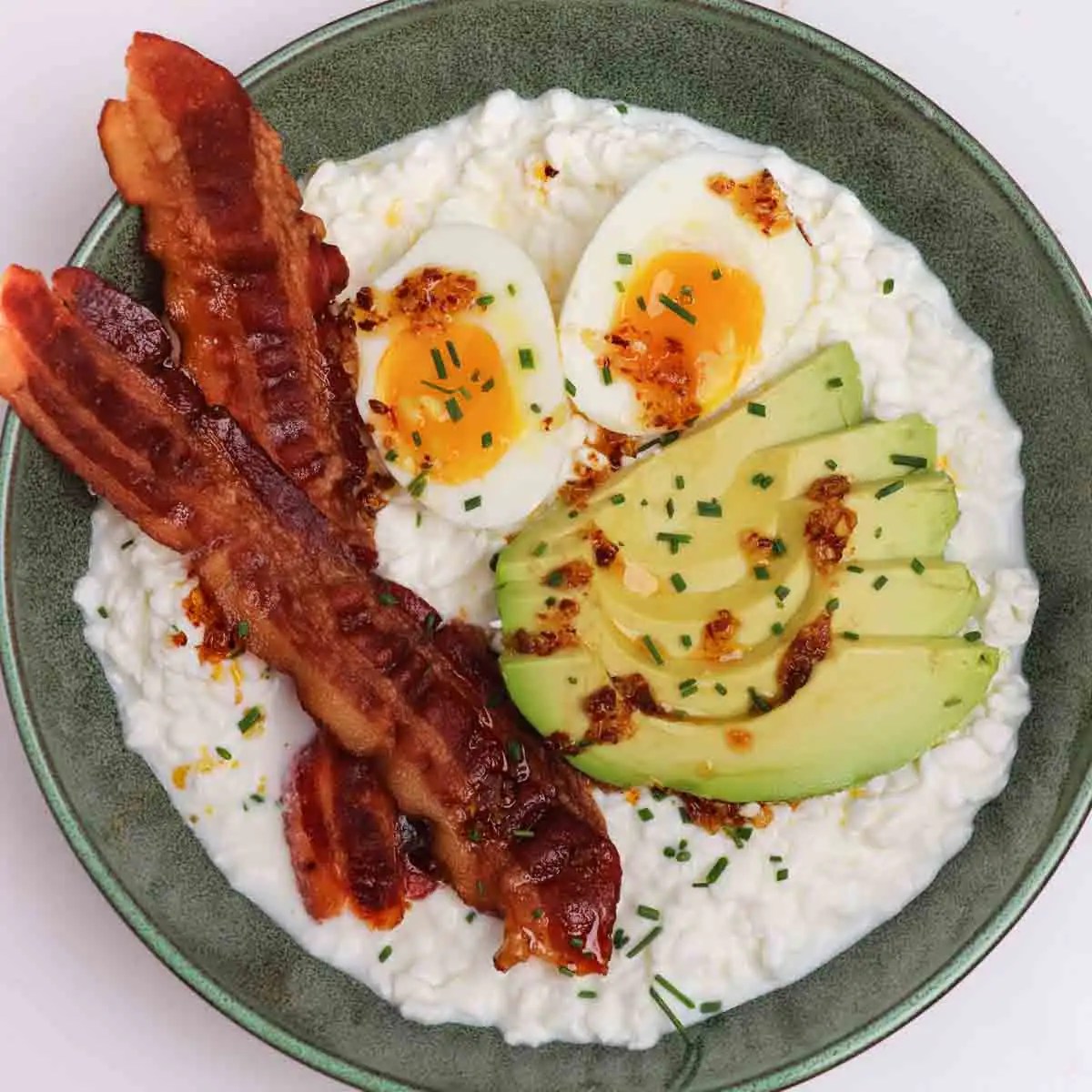 Cottage cheese bowl filled with soft boiled egg, sliced avocado, bacon, and chili crisp.