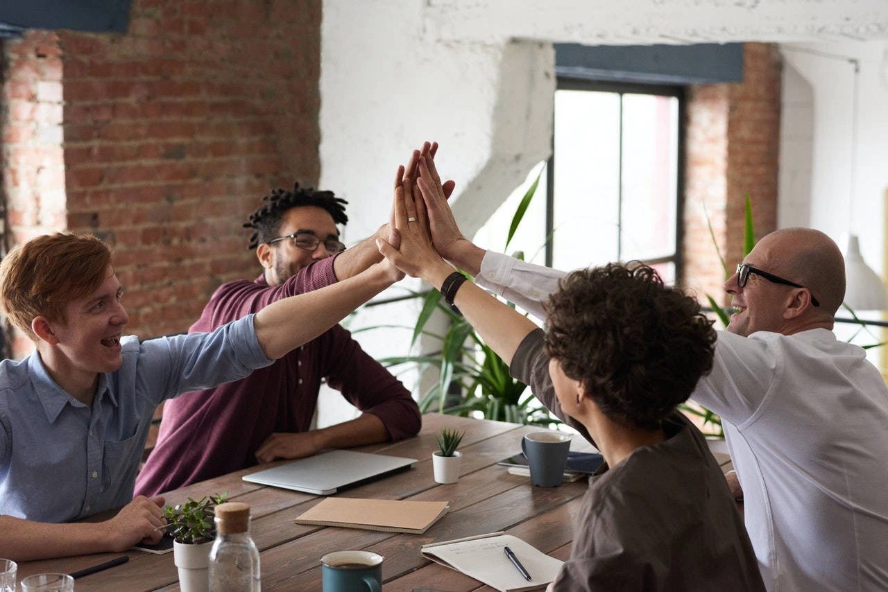 Photo of group high-five around a table.