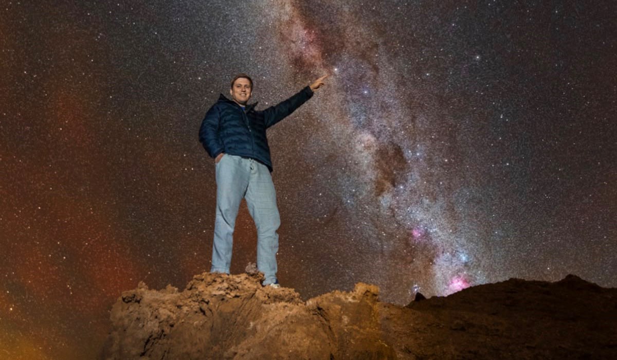 Philip Johnston pointing at Alpha Centauri in the night sky from an outcrop in the Atacama Desert