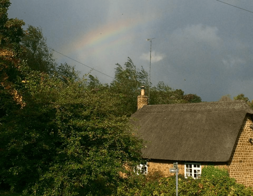 A home in England with a rainbow above it in the sky.