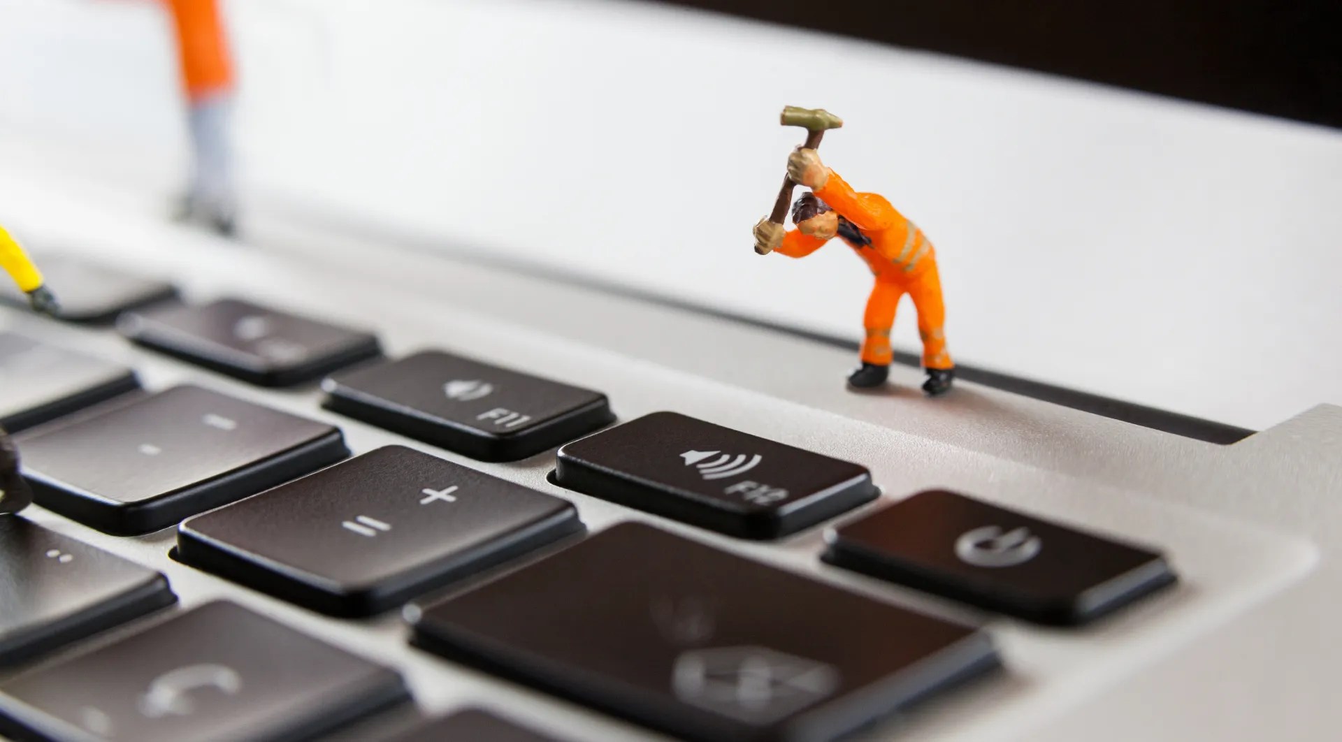 photo of a small toy with a hammer hitting a laptop keyboard