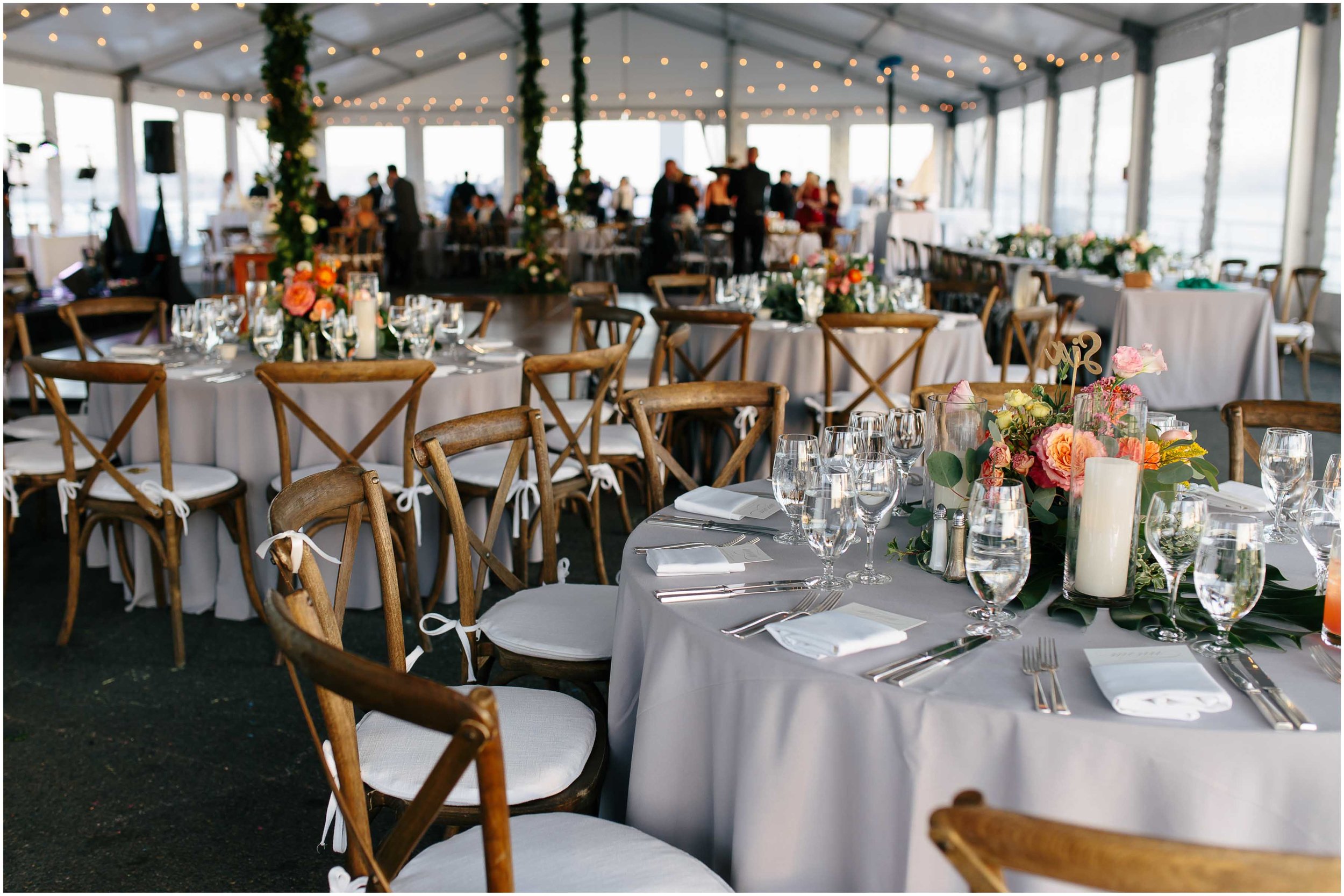 Elegant dining setup at an event on Pier 4, featuring tables with floral centerpieces, glassware, and wooden chairs under a marquee structure.