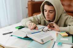 young man in beige hoodie reading and studying at home