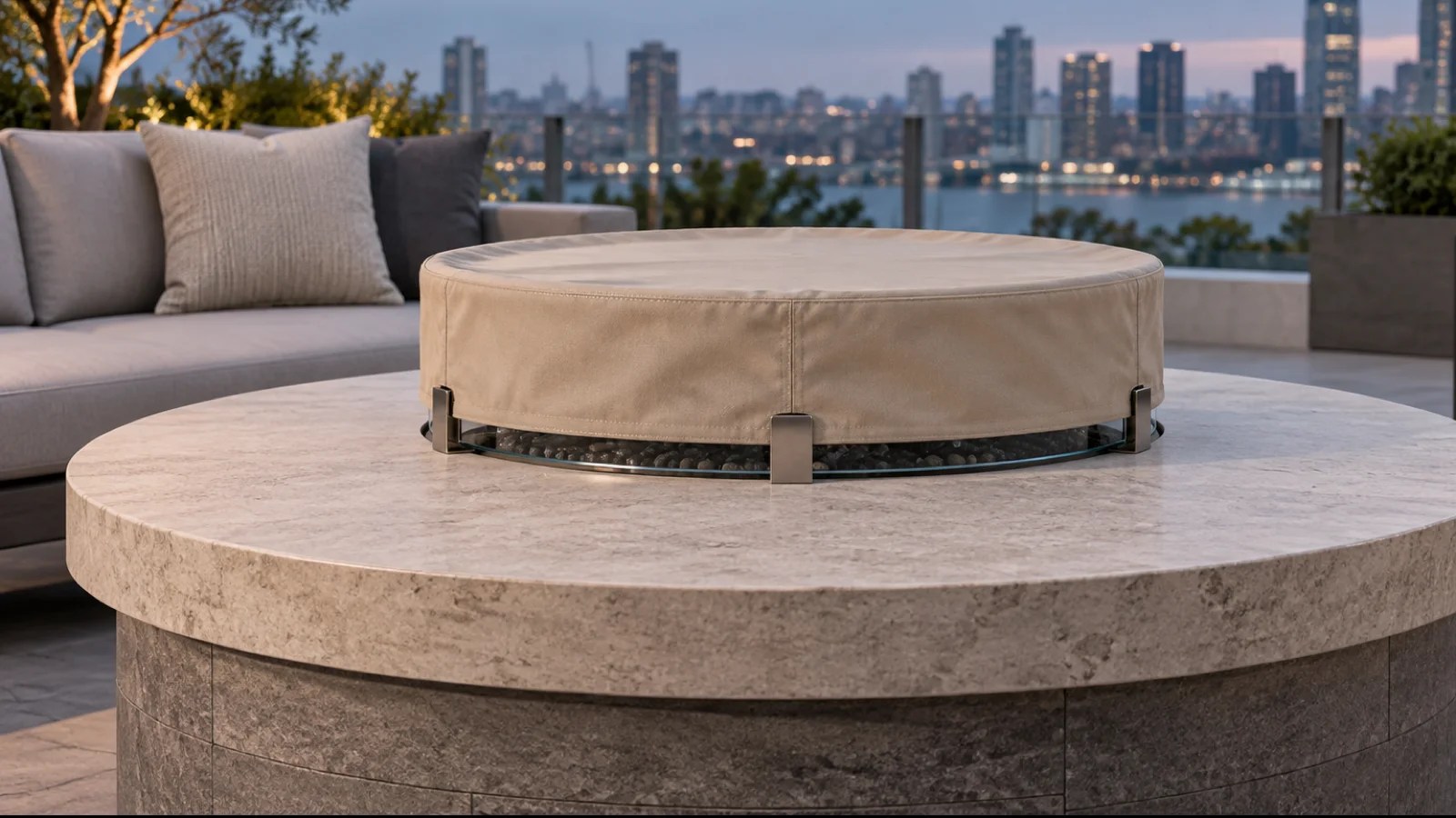Sand-colored fitted cover protecting a circular glass fire pit wind guard after the burner has cooled on a modern patio