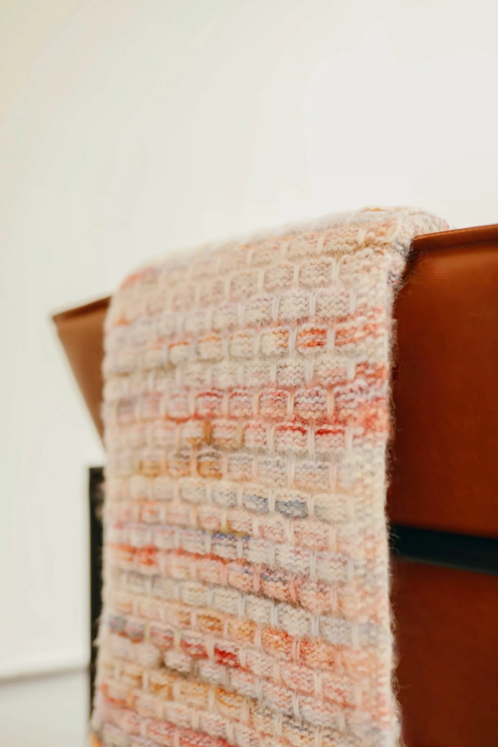 Blanket folded over the back of a leather chair. Handmade knit blanket that is cream, red, and blue.