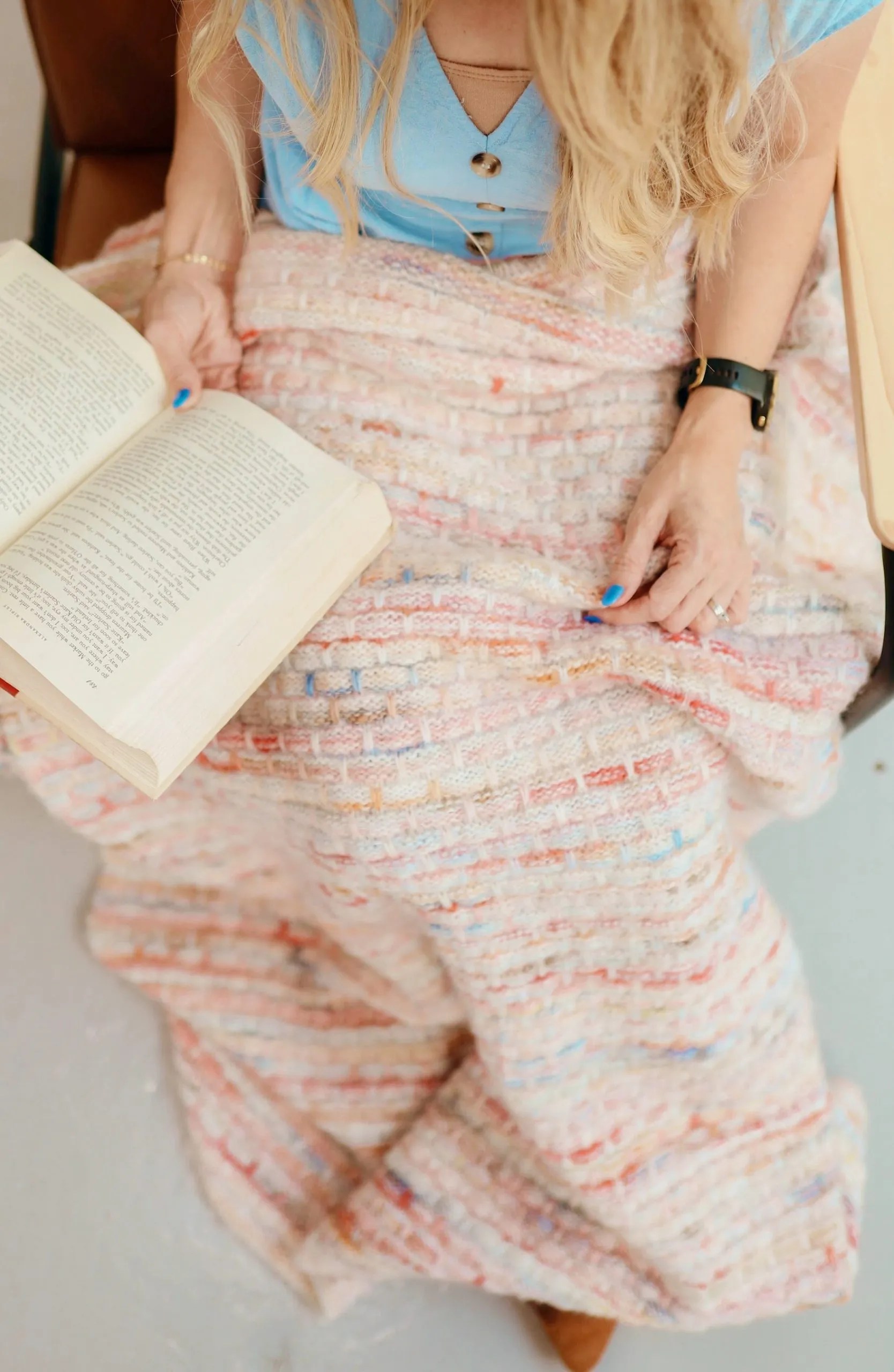 Woman in a blue dress reading a book with a handmade knit blanket on her lap