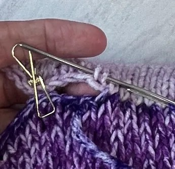A clip is holding the two sides of a pillow together as it is demonstrated how to sew the knit panels together