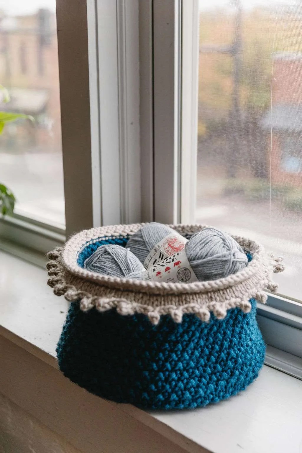 Knit basket filled with yarn sitting on a windowsill.