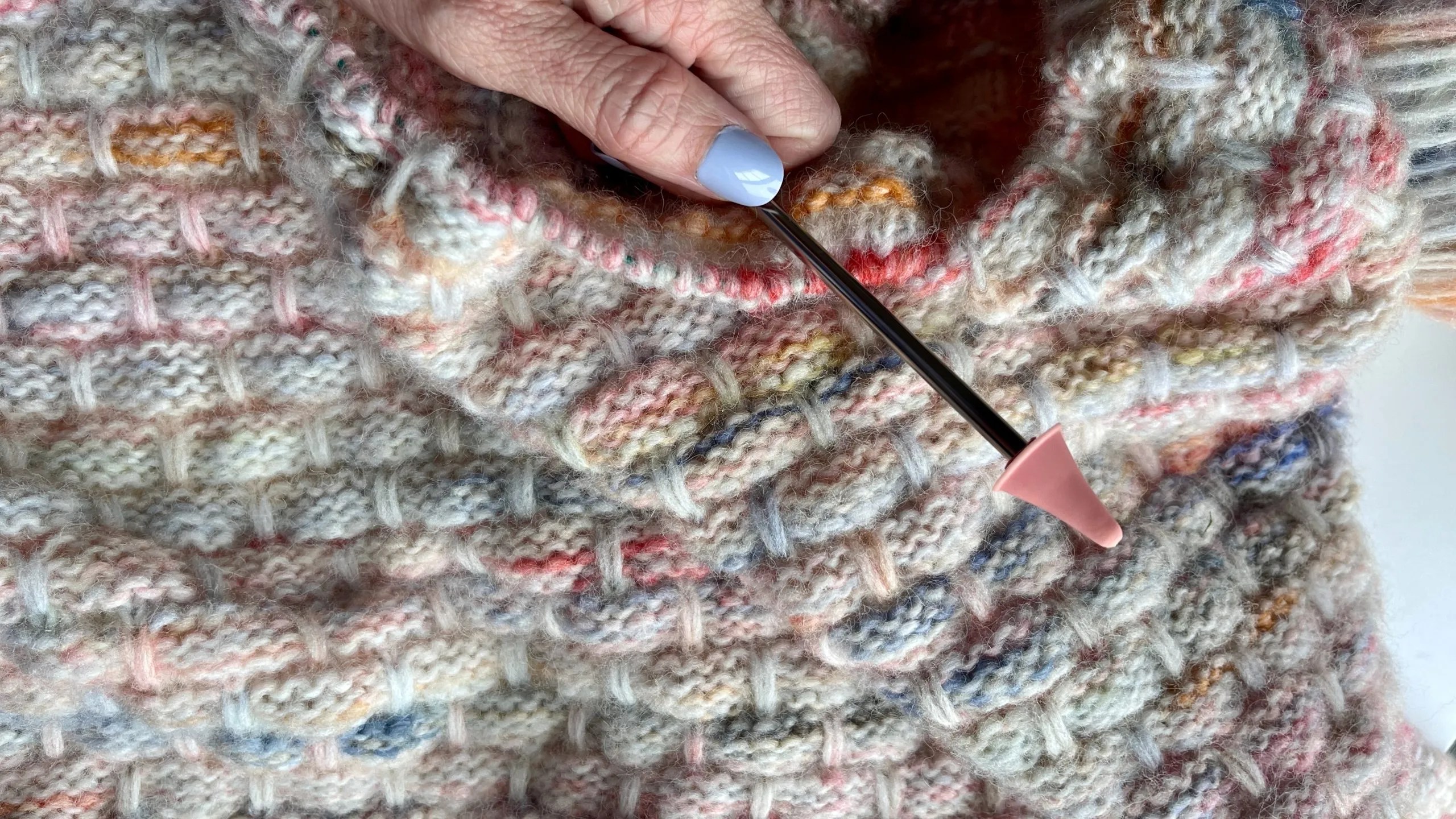 Hand showing a knitting needle and a blanket being made that has a brick pattern on it.