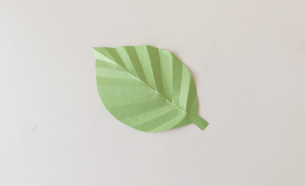 Folded green paper leaf with accordion creases for the moving caterpillar craft.