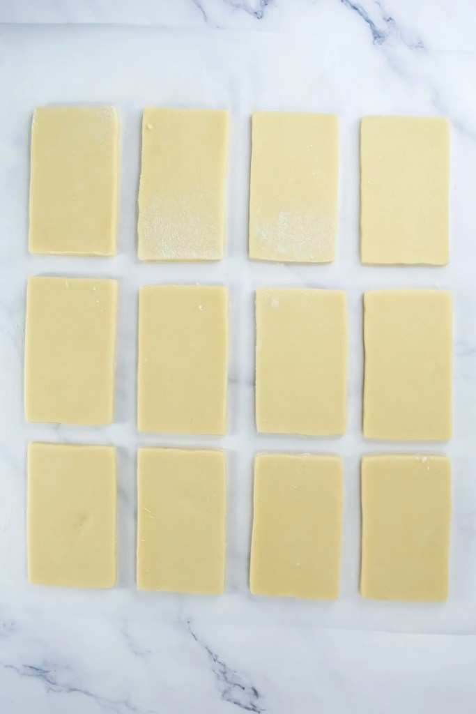 Rectangular cookie shapes cut from dough and placed on parchment for baking.