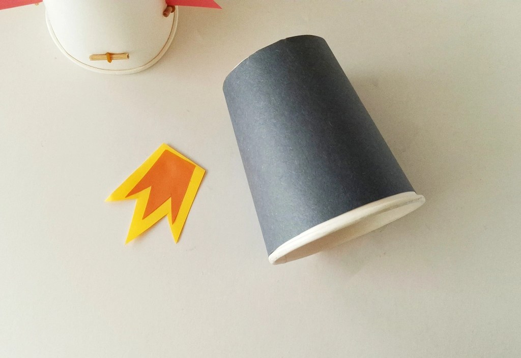 Black paper-covered paper cup and layered paper flames ready to assemble the rocket launcher.