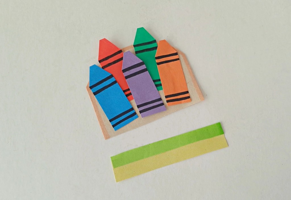 Paper crayons arranged in their holder with strips ready to cover the bottom.