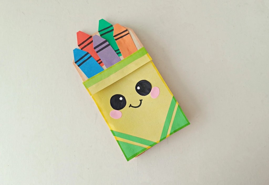 Finished yellow crayon box paper bag puppet filled with colorful paper crayons.