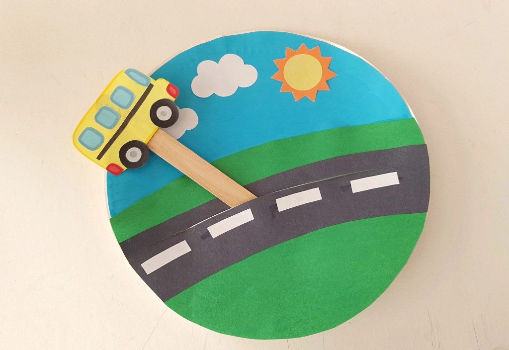 Popsicle stick inserted through the slit in the paper plate so the school bus can slide along the road.