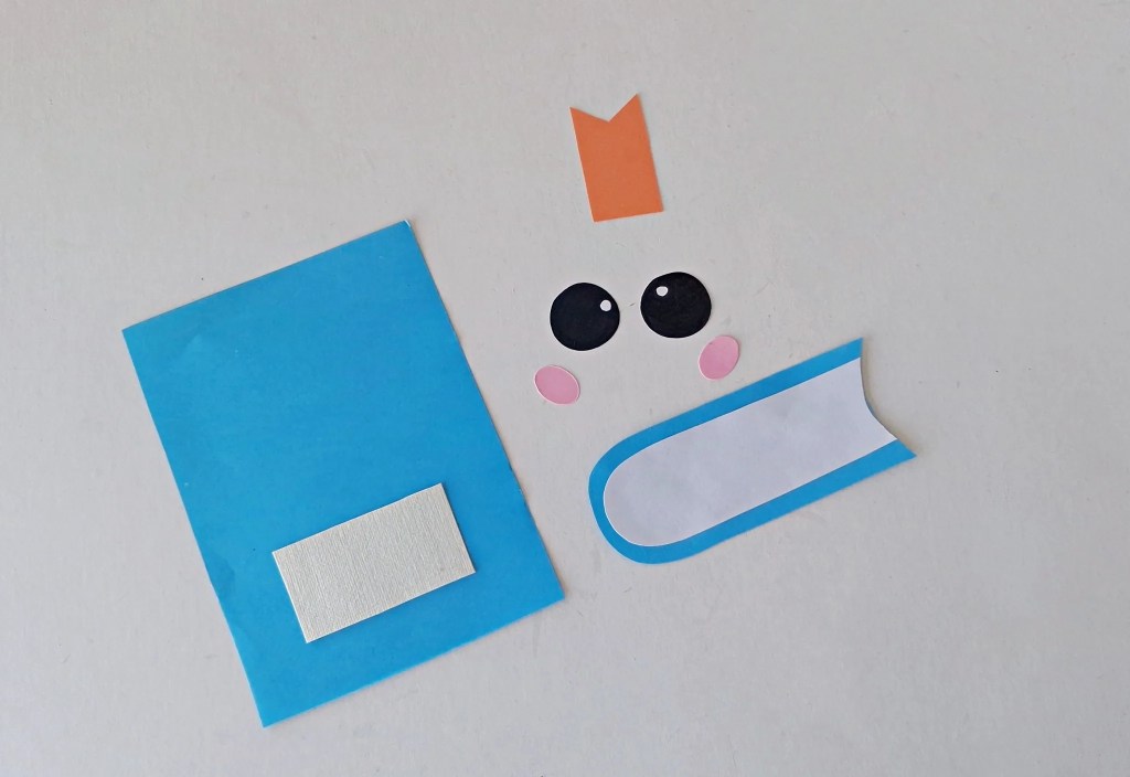 Blue notebook, page, bookmark, face, and label pieces being assembled.