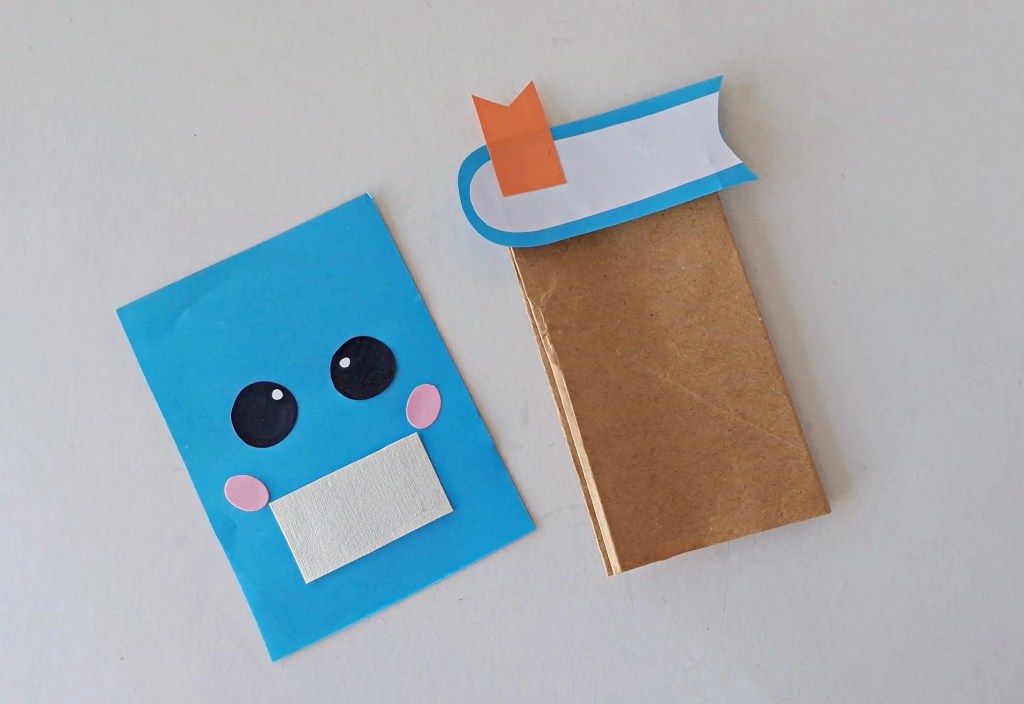 Blue notebook pieces being attached to a brown paper bag.