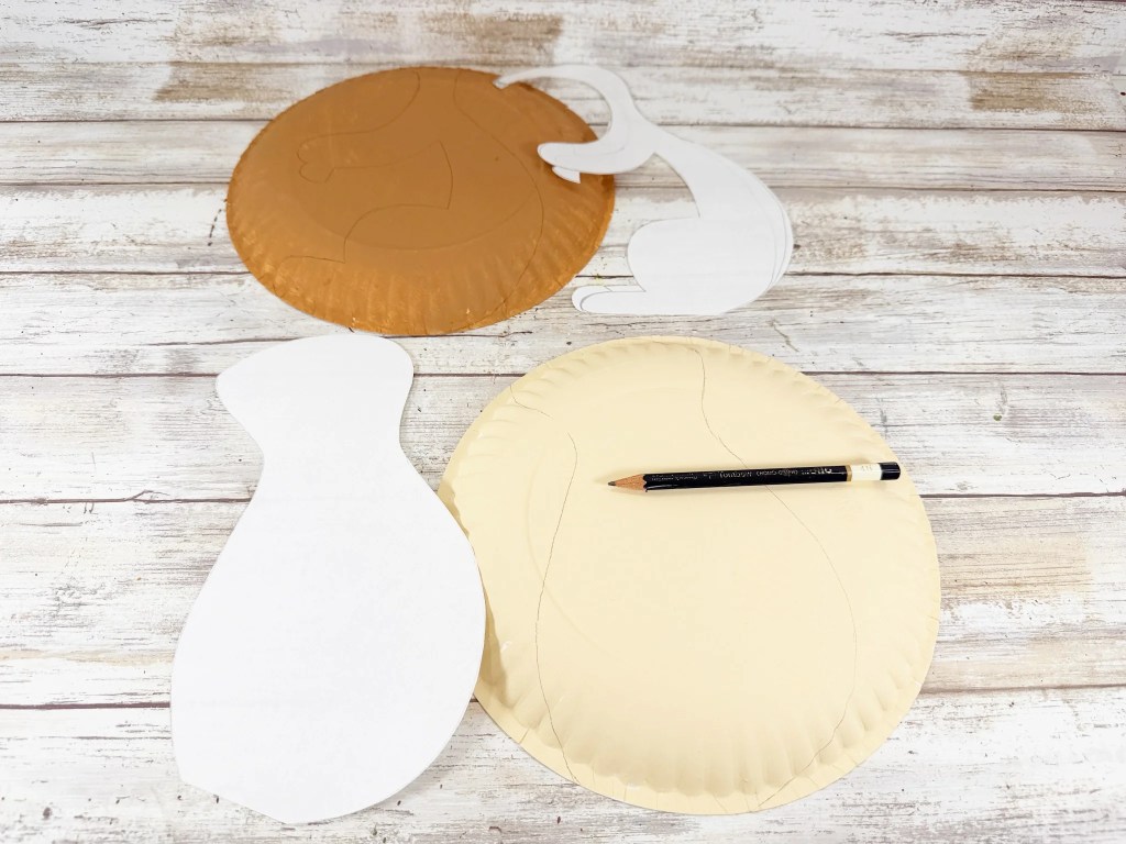 Squirrel body patterns being traced onto painted paper plates with a pencil.