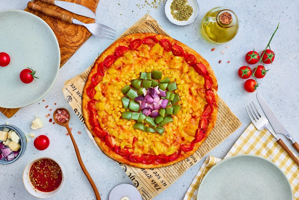 Baked rainbow veggie pizza with colorful vegetable rings and melted cheese