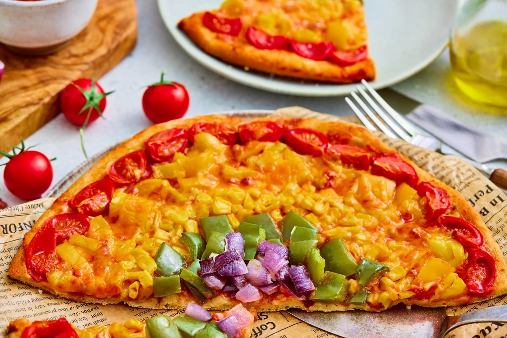Close-up of baked rainbow veggie pizza topped with colorful vegetables and cheddar cheese