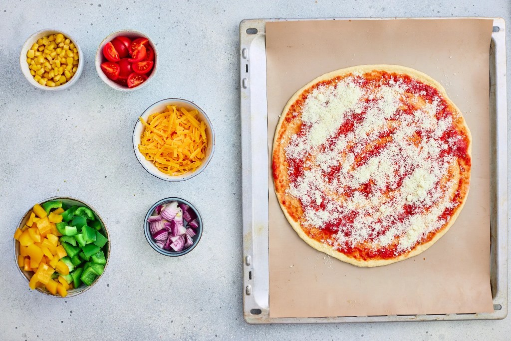 Parmesan cheese sprinkled over tomato sauce on pizza dough