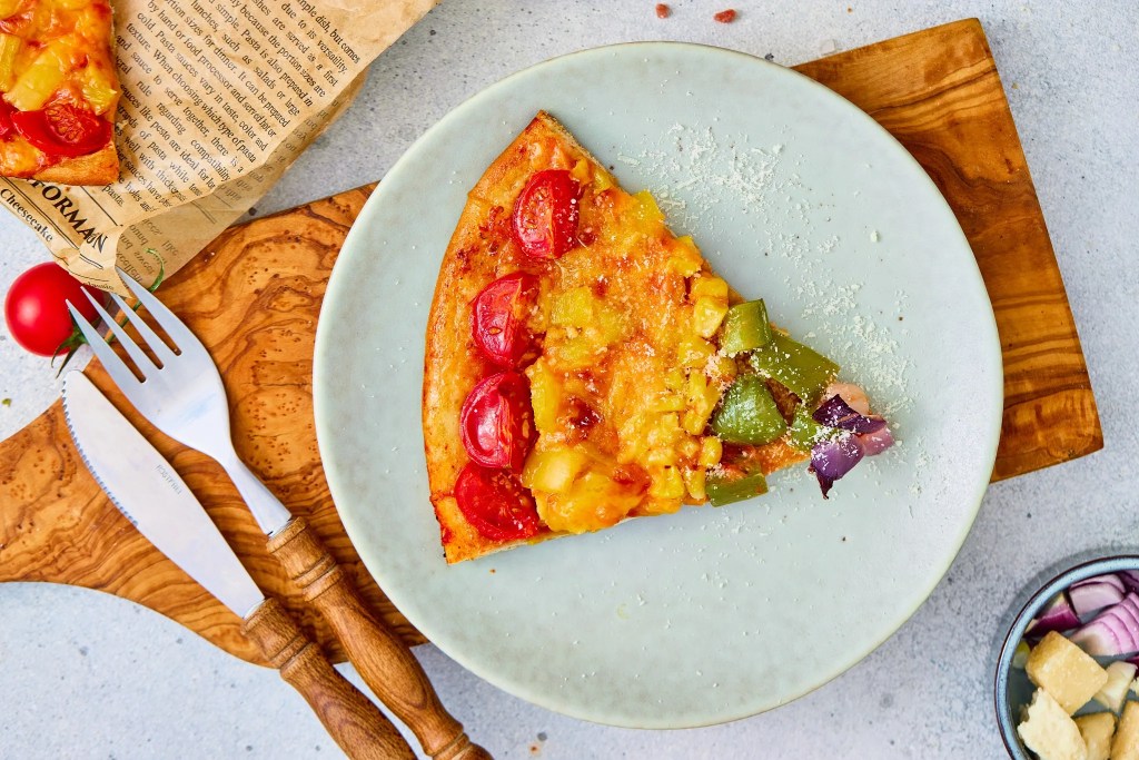 Slice of rainbow veggie pizza with tomatoes, peppers, corn, onion, and melted cheese
