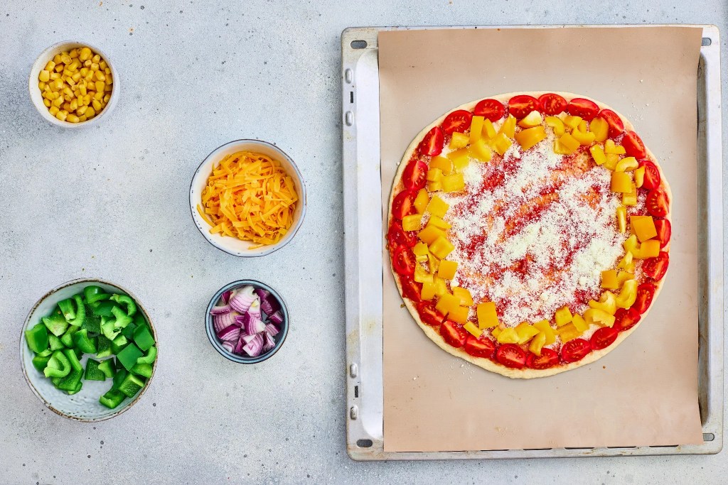 Cherry tomatoes and yellow bell pepper arranged in colorful rings on veggie pizza