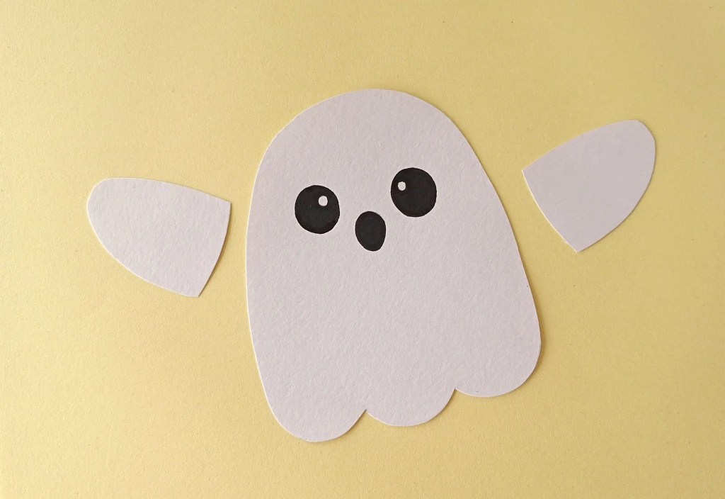 Face drawn on the white paper ghost with two arm pieces beside it