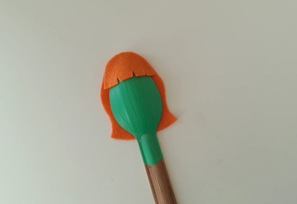 Orange felt bangs attached to the top of the painted spoon.