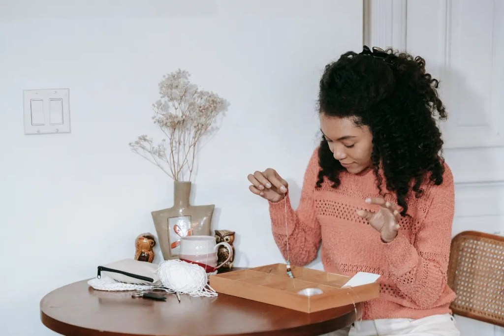 Woman seated at home threading beads while working on a jewelry-making project.