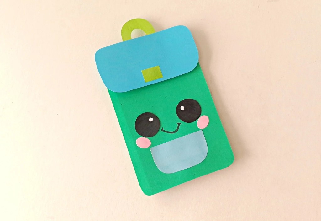 Finished green paper bag backpack puppet with blue flap and pocket.