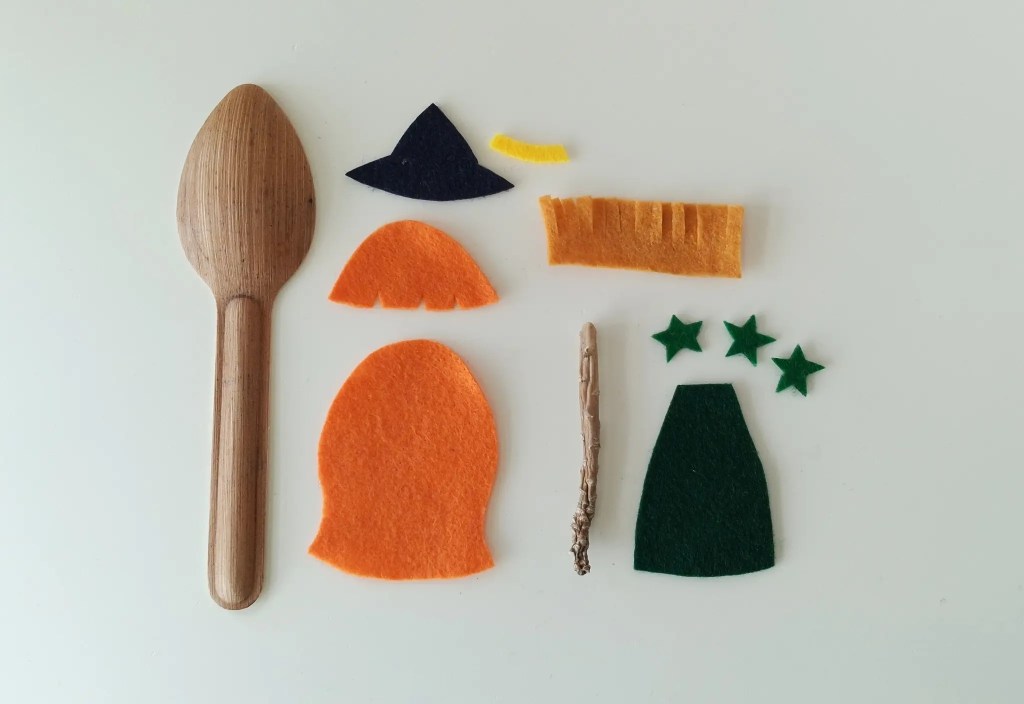 Wooden spoon with colourful felt pieces, a twig, and witch craft decorations.