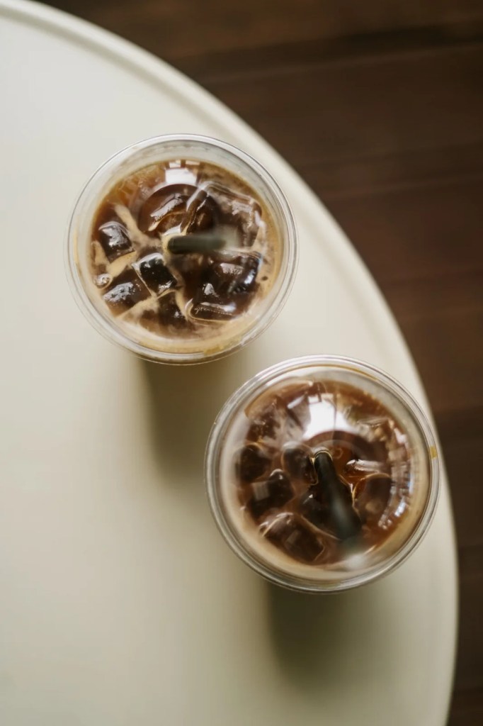 Overhead view of two iced coffees with ice and straws on a light-colored table.