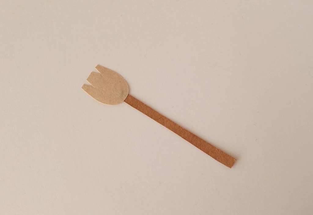 Brown paper broom handle attached to a beige paper broom head for a flying witch craft.