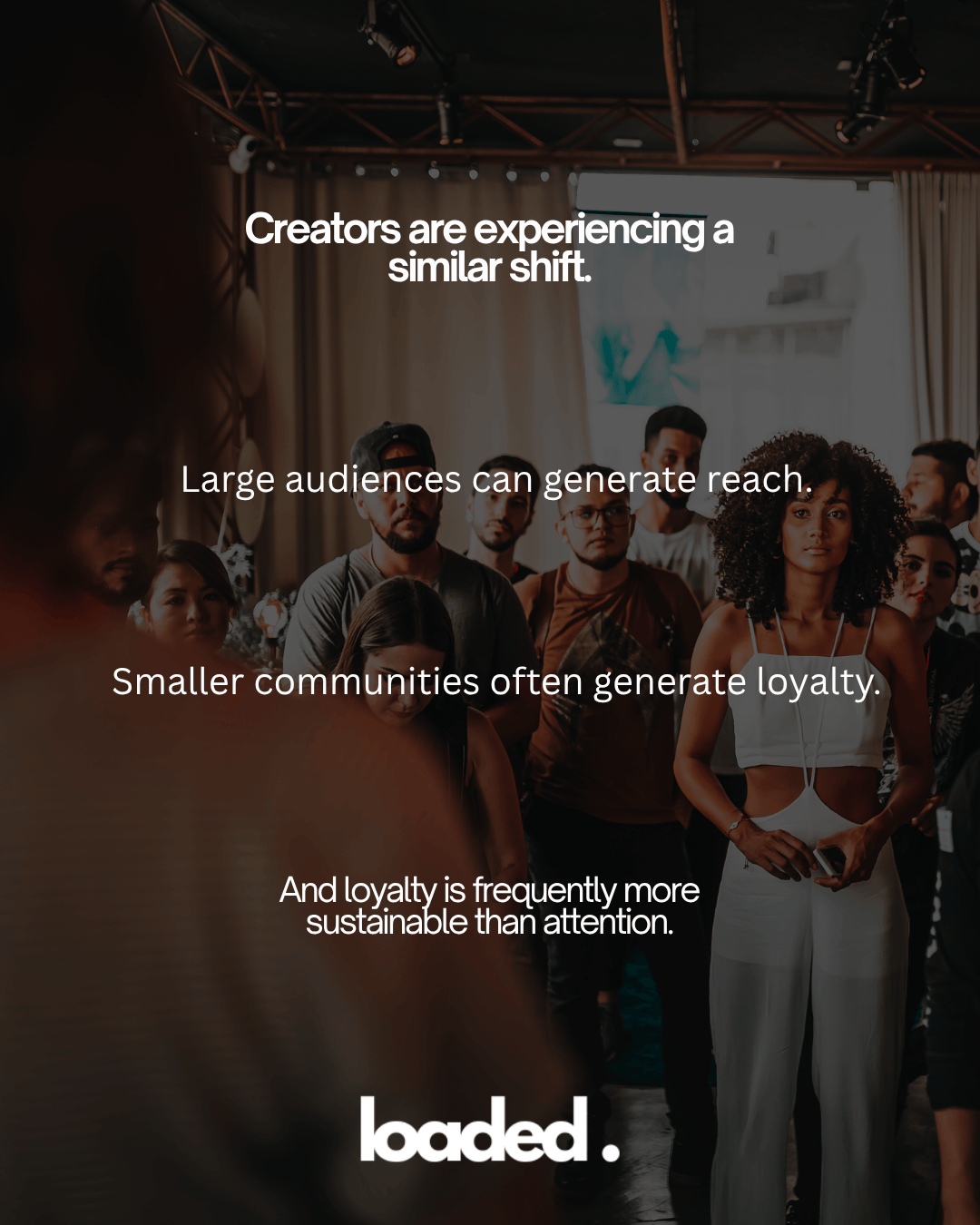 A diverse group of people gathered in a well-lit space, focusing attentively on a speaker, with text overlay discussing the importance of community and loyalty for creators.