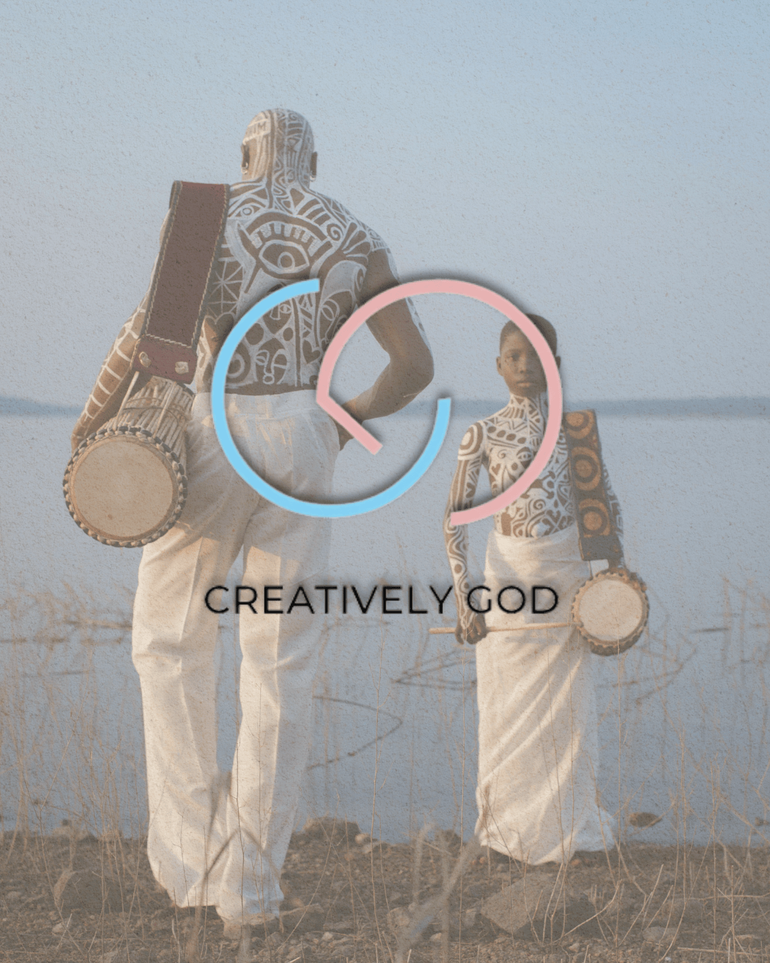 A man and a woman walking side by side near a body of water, both carrying drums. They are adorned with intricate body art and wearing white clothing. The image has a muted background with a logo overlay that reads 'CREATIVELY GOD'.