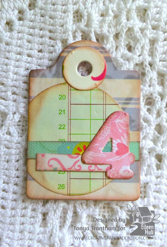 A decorative tag featuring a large number 4, set against a background with a grid pattern and floral accents, mounted on a textured white surface.