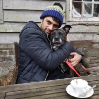 Man wearing black coat and beanie hugging a black dog.