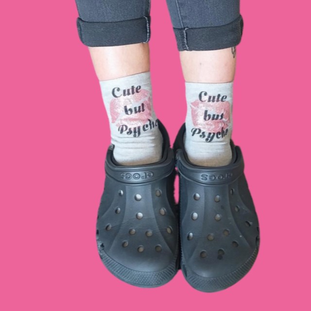 2 feet both wearing black Crocs and grey socks, reading cute but psycho