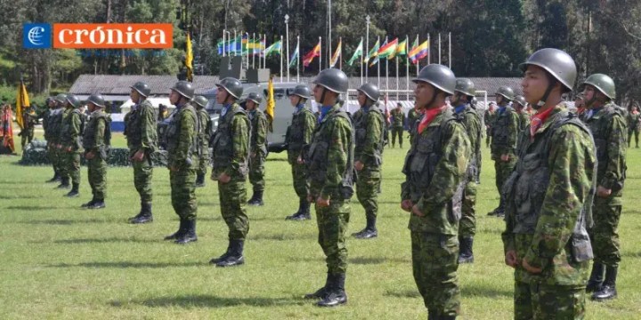 Ceremonia militar en el Fuerte Militar 'Miguel Iturralde', donde jóvenes conscriptos en formación presentan una formación con uniforme militar y casco, mientras se entregan armas. Banderas de diferentes países ondean al fondo.