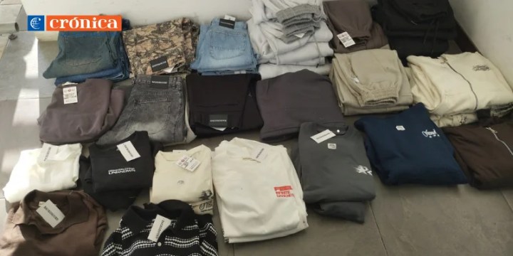 A neatly arranged display of various clothing items including jeans, shirts, and hoodies, all with tags still attached, laid out on a flat surface.