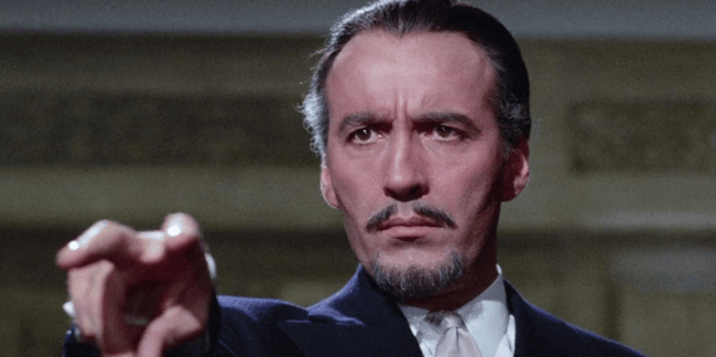 A close-up of a man in formal attire, pointing assertively with a serious expression on his face.