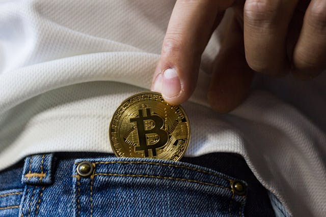 A man putting a physical Bitcoin in his jeans’ pocket.