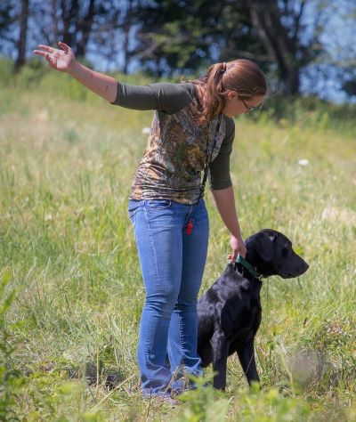 Woman standing next to a dog with her arm outstretched