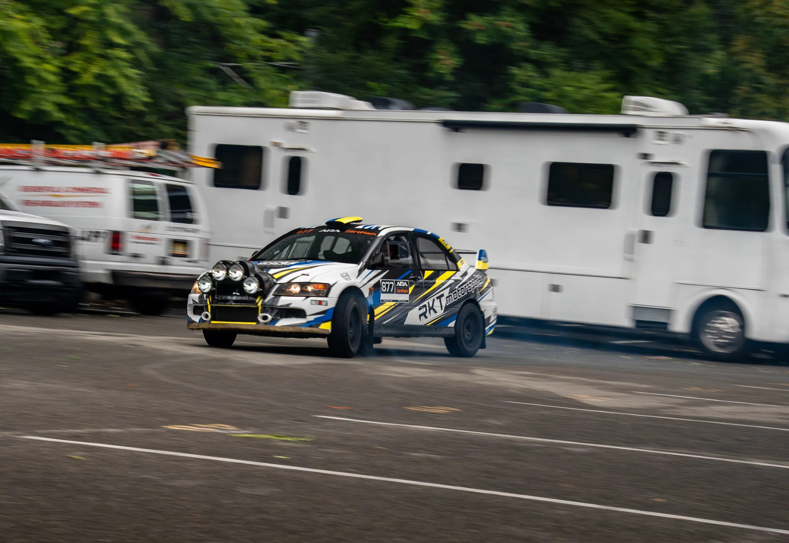 Evo 8 rally car rolling shot in the rain with motion blur past a white trailer